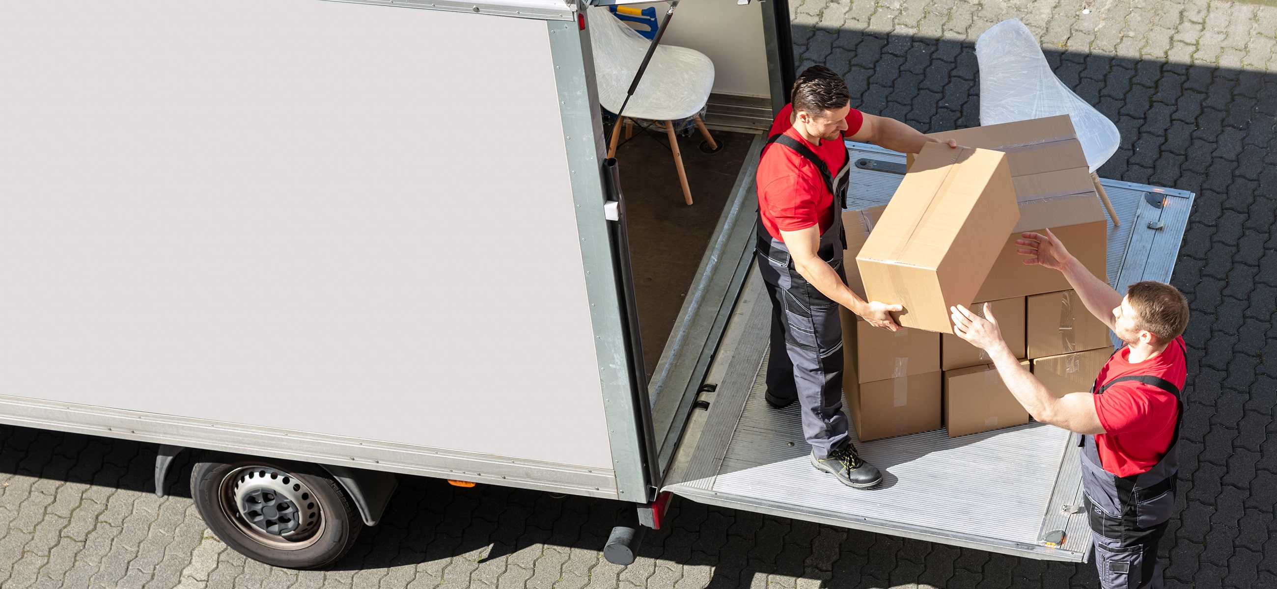 zwei Umzugshelfer laden Umzugskartons aus einem LKW aus